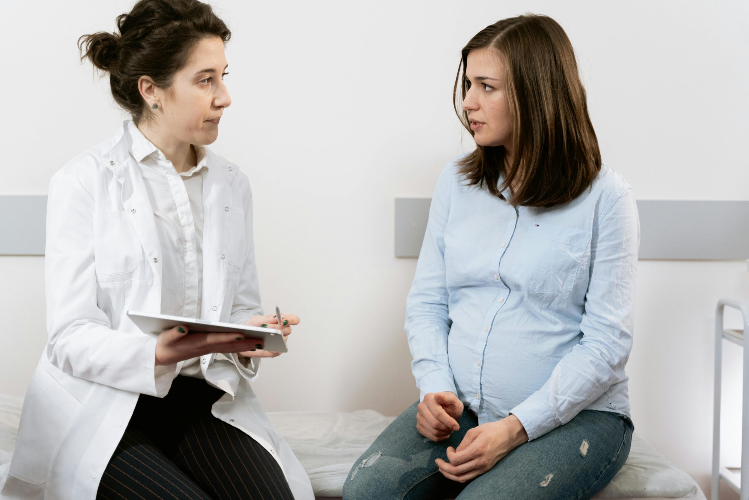 A pregnant woman consulting with a female doctor in a medical clinic setting.